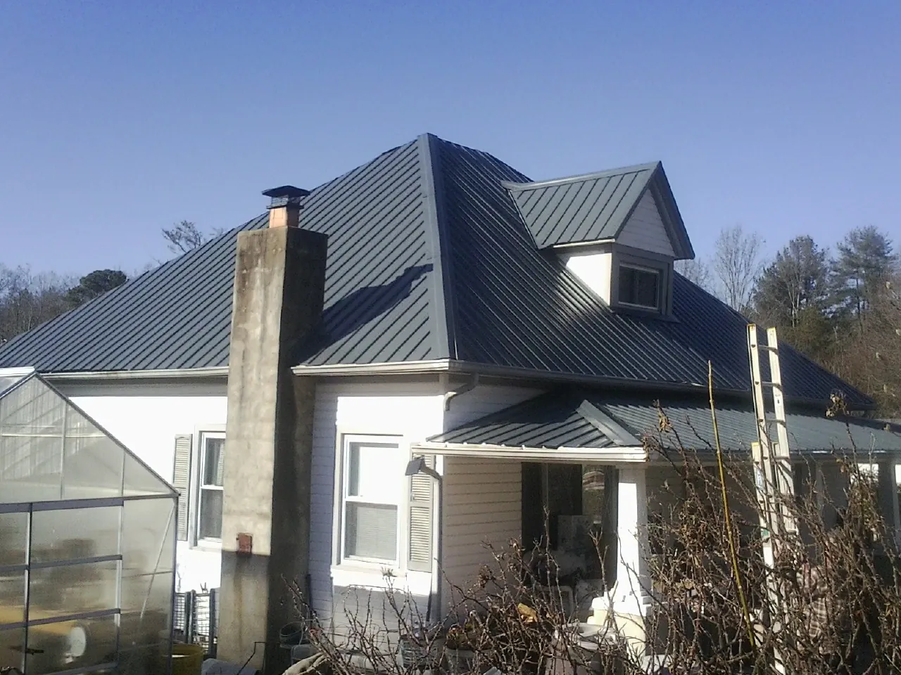 Dark blue standing seam metal roof on a white farmhouse with dormer — Slate & Tile Roof Repair by Roofing Brothers in Clarissa