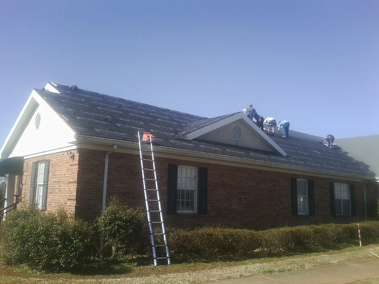 Crew tearing shingles off a brick ranch roof with a ladder set — Metal Roof Repair work by our crew in Clarissa