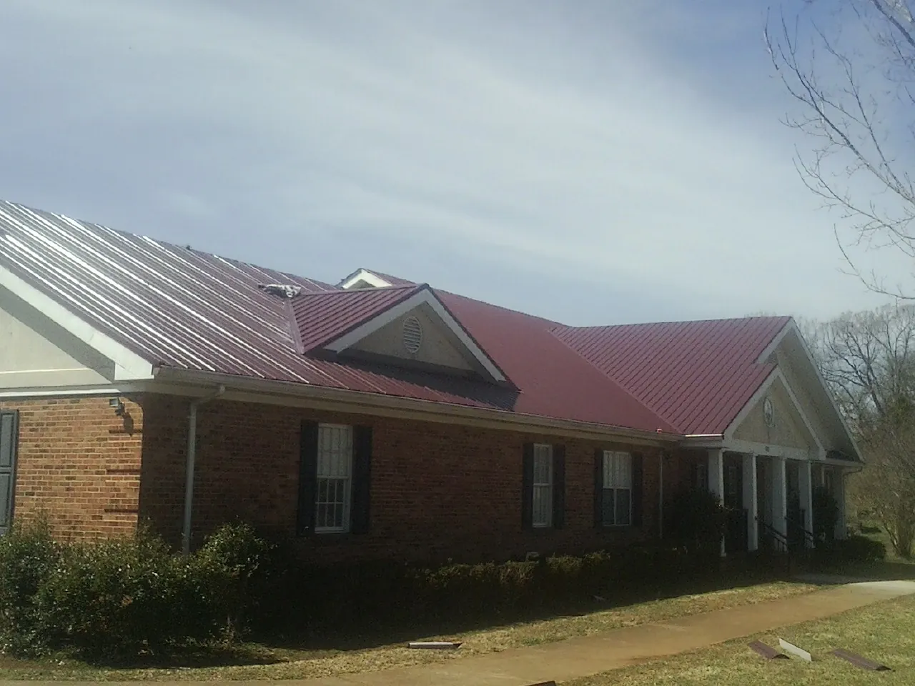 Red metal roof with gabled entries on a long brick building, from a Hail Damage Roof Repair job in Clarissa