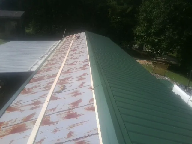 Old rusted panels beside newly installed green metal roofing — Wind Damage Roof Repair by Roofing Brothers in Clarissa