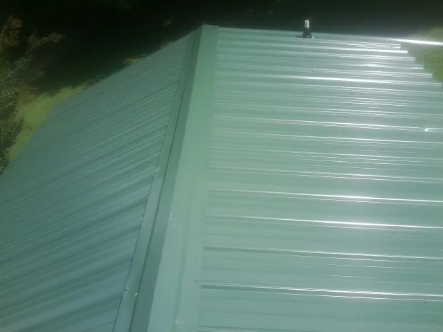 New green metal panels meeting at the ridge of a roof — Flat Roof Repair work by our crew in Clarissa
