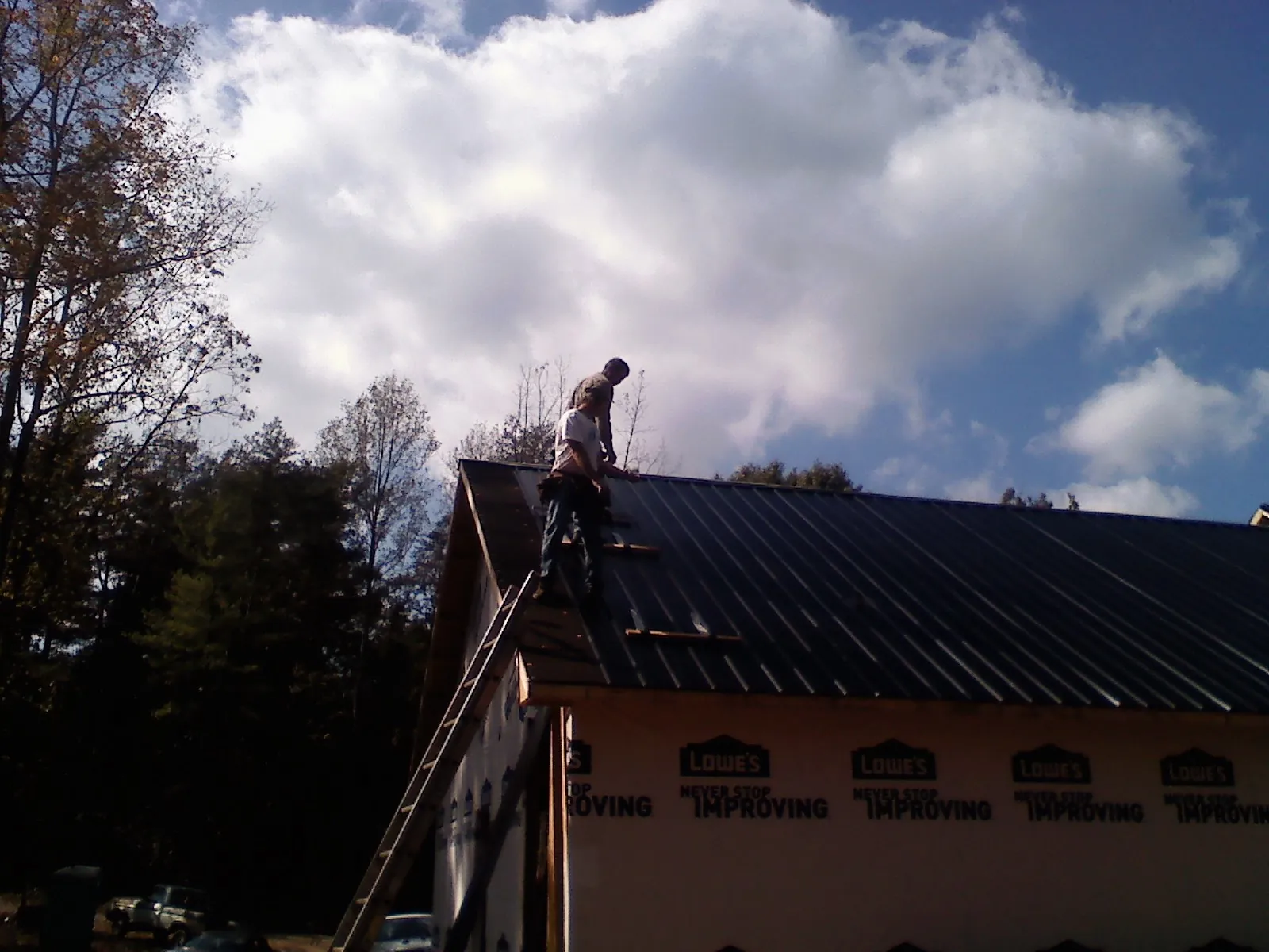 Roofer fastening dark metal panels high against a cloudy sky, from a Roof Inspection job in Clarissa