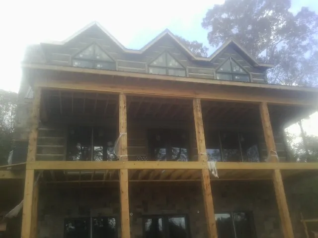 Dormers and porch framing on a large log home under construction — Roof Coating work by our crew in Clarissa
