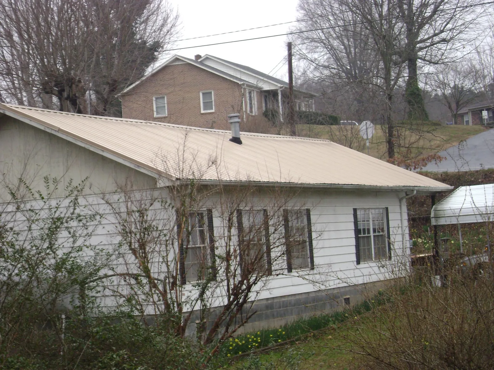 Tan metal roof on a white sided house set into a hillside — Commercial Roofing by Roofing Brothers in Clarissa