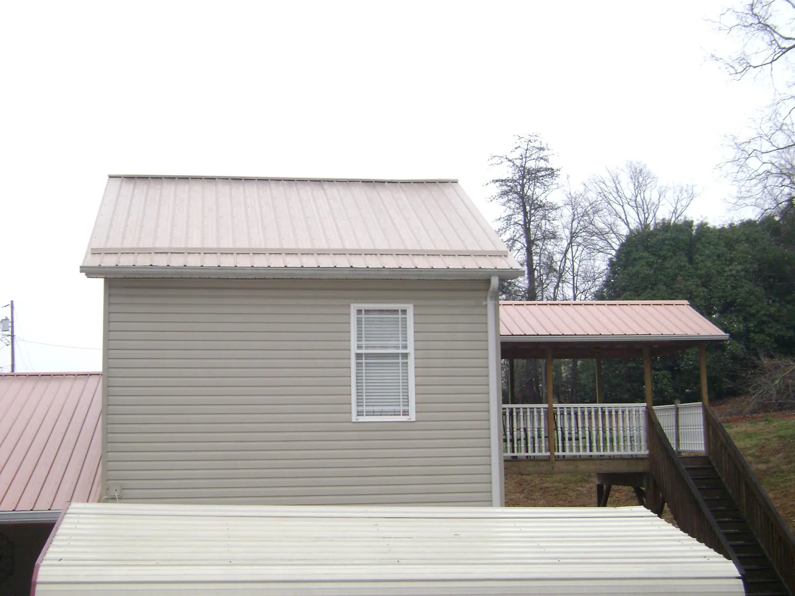 Tan metal roofs on a two story addition and attached porch, from a Roof Replacement job in Clarissa